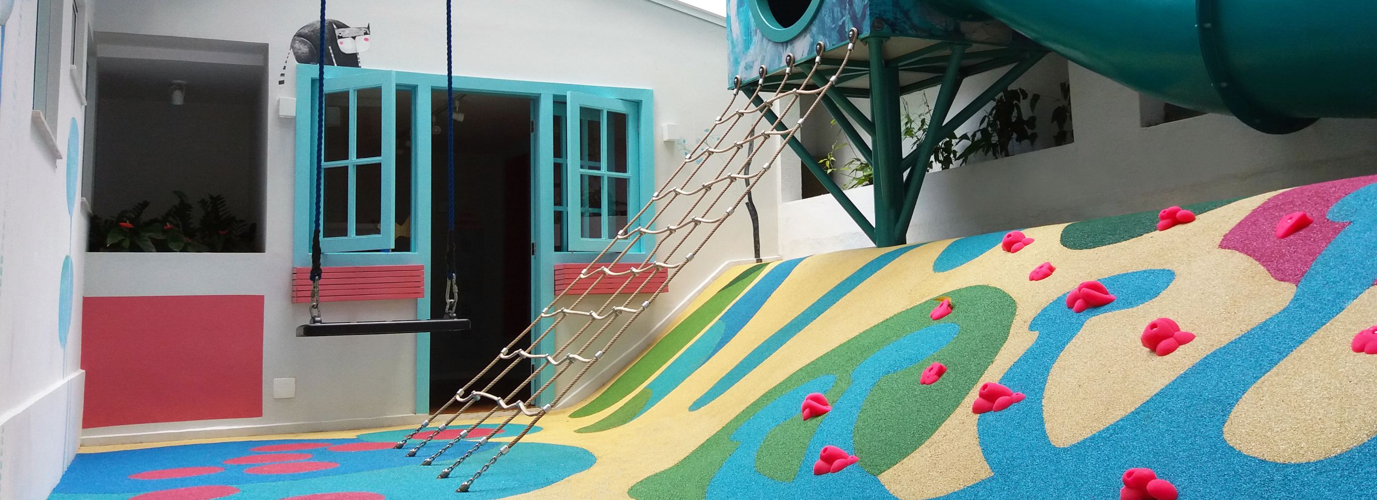 Outdoor playground built into a small courtyard with a rope climbing frame.