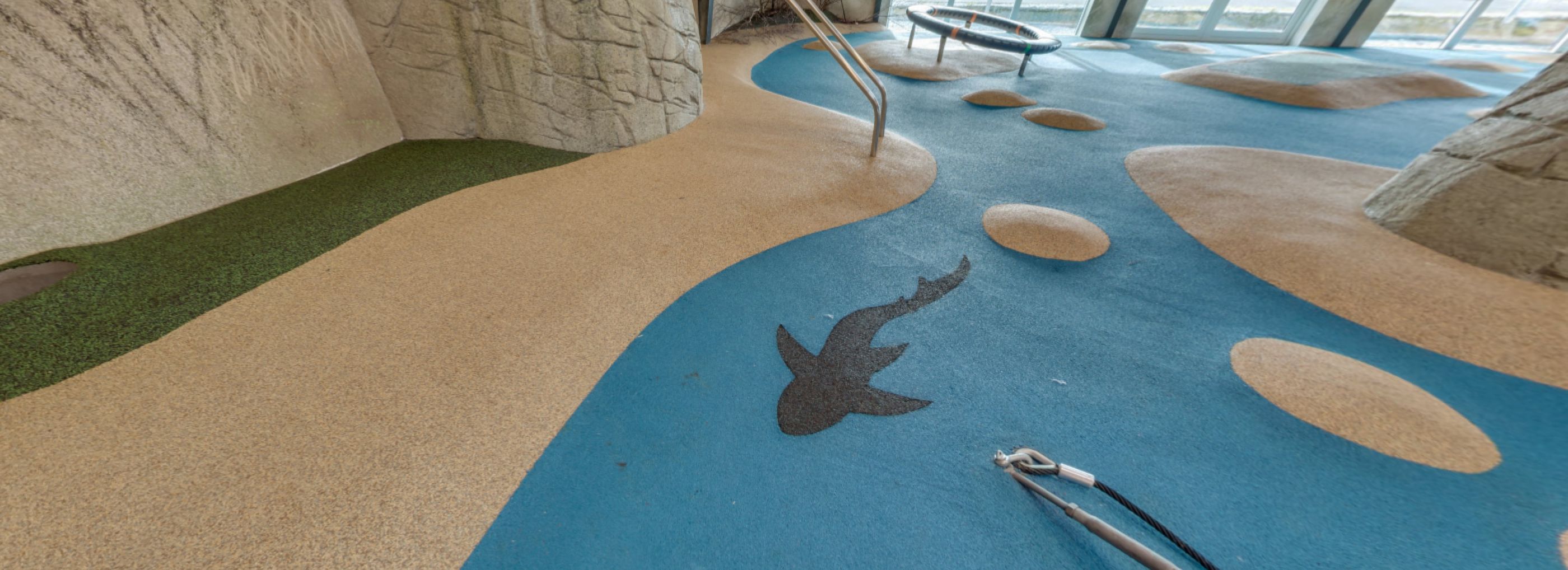 Indoor playground designed to look like a beach with a blue colour for water and sandy brown colour for the beach with a silhouette of a shark in black.