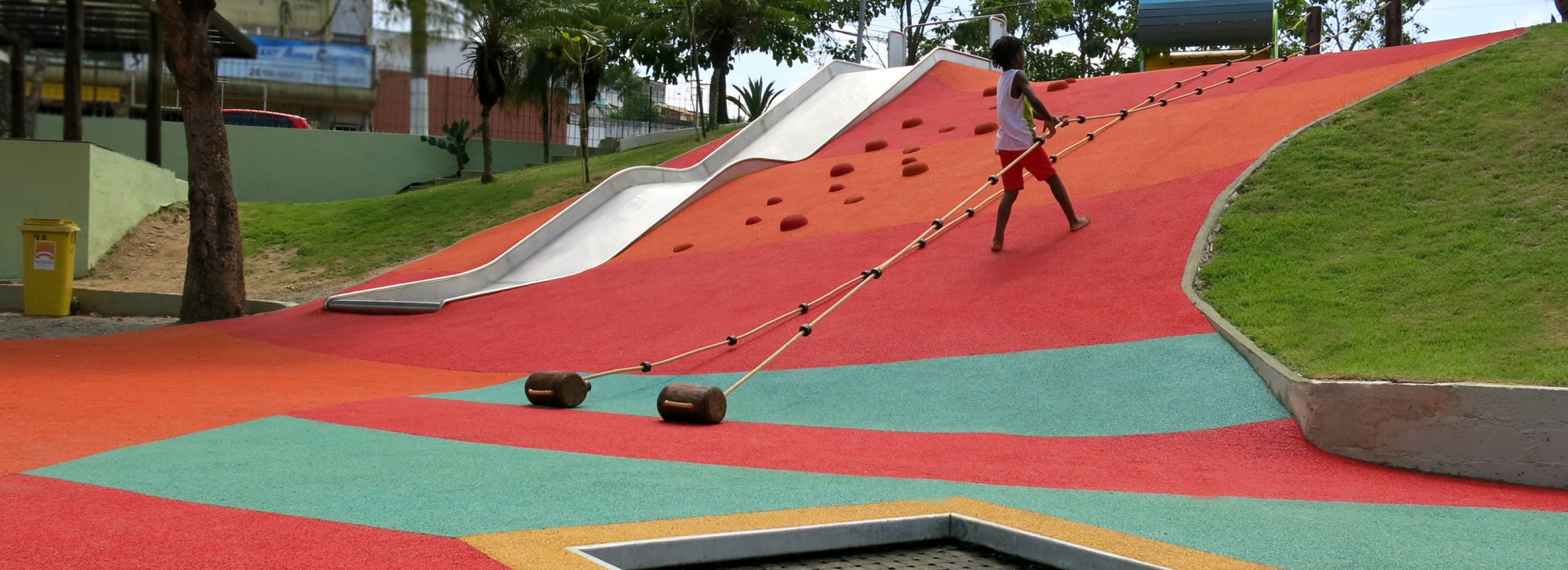 A kid climbing up a hill that has been covered in a colourful rubber flooring.